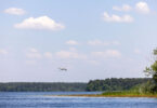 A heron flys over a body of water on a pretty day.