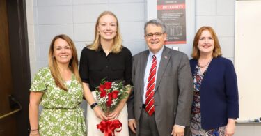 UGA President Jere W. Morehead and Morehead Honors College Dean Meg Amstutz stand with senior Sadie Bengs, holding a bouquet of red roses, and Maryann Gallagher, director of the Richard B. Russell Security Leadership Program, after surprising Bengs in class with the announcement that she is a 2025 Truman Scholar.